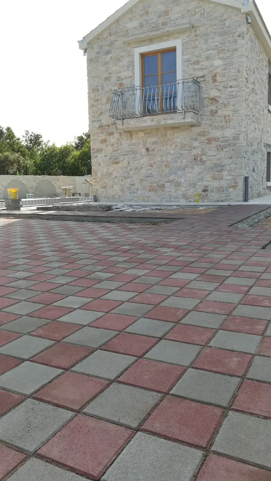 Popločano dvorište uz kamenu kuću crveno-sivim opločnicima u kockastom uzorku